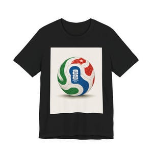 May include: A black short-sleeve t-shirt featuring a centered rectangular graphic of a soccer ball. The ball displays green, red, and blue swirling patterns with a white star and the text FIFA WORLD CUP 2026 printed in blue on a white background.