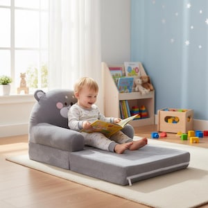 May include: A grey plush foam chair that unfolds into a floor mat, featuring a stylised bear face on the backrest with rounded ears, a white muzzle, and pink cheeks. The soft, cushioned seat is designed for children to sit or lounge comfortably.