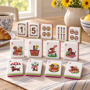 Puede incluir: Un juego de fichas de mahjong rectangulares blancas con ilustraciones coloridas de perros salchicha, cestas de picnic, flores y sombrillas, algunas con la letra F o los números 1 y 5, con bordes superpuestos en verde y rosa.