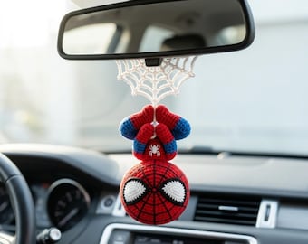 Peut inclure: Une décoration suspendue en crochet représentant un personnage de super-héros rouge et bleu accroché à une toile d'araignée en fil blanc. Le personnage a une tête ronde avec de grands yeux blancs, un motif de toile noire et un petit emblème d'araignée blanc sur la poitrine.