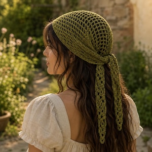 Può includere: Un foulard all'uncinetto color verde oliva caratterizzato da un motivo a rete traforato. Il foulard è annodato sulla nuca con due lunghe estremità pendenti che presentano anch'esse un motivo decorativo a punto traforato ripetuto.