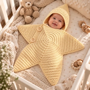 May include: A pale yellow crocheted star-shaped baby swaddle blanket with a pointed hood. The garment features two round wooden buttons on the front flap, allowing it to wrap securely around an infant. The texture is consistent throughout.