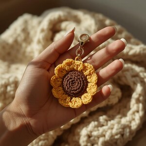 May include: A crochet sunflower keychain featuring a dark brown center and bright yellow petals. The flower is attached to a gold-toned metal lobster clasp and a circular ring, providing a functional attachment point for keys or accessories.