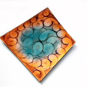 May include: A square tile with a swirling pattern in shades of orange, brown, and teal.