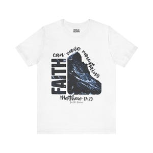 May include: A white short-sleeved t-shirt featuring a graphic of a dark mountain silhouette. The text reads "FAITH can move mountains" and "Matthew 17:20" in black lettering. The brand name "BIBLE BORN" is printed at the inner neckline and bottom.