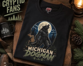 May include: A black t-shirt featuring a graphic of a werewolf howling at a full moon in a forest setting. The design includes the text MICHIGAN DOGMAN and a silhouette of the state of Michigan. The shirt has a crew neck and short sleeves.