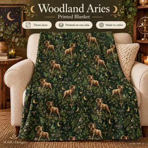 May include: A dark green blanket featuring a repeating pattern of rams, crescent moons, fern leaves, and the text Aries. The design includes small white flowers scattered throughout the foliage. The blanket is draped over a light-colored armchair.