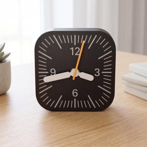 Könnte beinhalten: Eine quadratische Analog-Uhr mit schwarzem Zifferblatt, weißen Stundenmarkierungen und weißen Ziffern an den Positionen 3, 6, 9 und 12. Die Uhr hat zwei breite weiße Zeiger für Stunden und Minuten sowie einen dünnen, leuchtend orangen Sekundenzeiger.