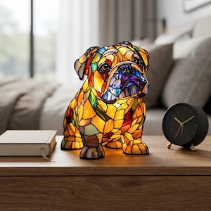 May include: A bulldog-shaped lamp constructed from numerous small, multi-coloured stained glass pieces in shades of amber, yellow, red, blue, and green. The lamp features a detailed face with dark eyes and a black nose, illuminated from within.