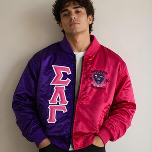 May include: A two-toned satin bomber jacket featuring a purple right side with large white and pink Greek letters and a pink left side with an embroidered crest and the text Culture Is Pride 1990 Pride In Success. The jacket has a black zip fastener.