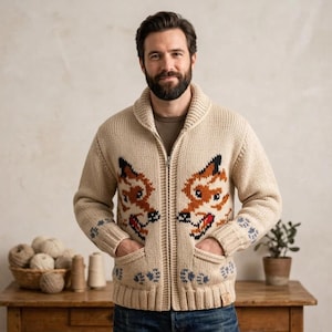 May include: A beige knit zip-up cardigan featuring a shawl collar and a repeating fox face pattern in orange, black, and white. The garment includes two front pockets and blue paw print accents near the cuffs and hem, with a ribbed texture.