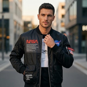 May include: A black bomber jacket featuring a NASA logo on the chest and sleeve, with white text detailing the National Aeronautics and Space Administration. The jacket includes a front zipper, two flap pockets, and a small American flag patch.