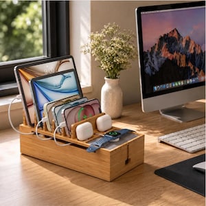 May include: A rectangular bamboo charging station with multiple slots for tablets and smartphones. The organiser features integrated white charging cables, two white wireless earbud cases, and a blue smartwatch resting on a flat surface.