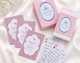 May include: A deck of playing cards with pink and white striped packaging and individual cards featuring a scalloped white label with the text David & Jessica 08.29.2026. One card displays the number 4 of diamonds and a printed quote about love.