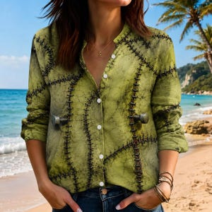 Può includere: Una camicia a maniche lunghe con bottoni in tessuto testurizzato verde chiaro, caratterizzata da un motivo scuro a crepe e file verticali di cuciture nere. Due protuberanze metalliche simili a bulloni sono fissate sul davanti della camicia.