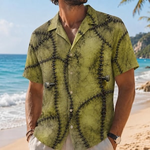 Puede incluir: Una camisa de manga corta con botones en color verde oliva pálido con un patrón de superficie texturizado y moteado. La camisa presenta un estampado gráfico de costuras oscuras sobre la tela y dos iconos de pernos metálicos en la parte frontal.