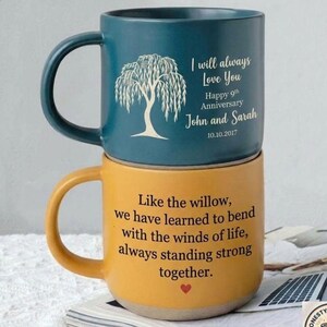 May include: A dark teal mug stacked on a mustard yellow mug. The teal mug features a white willow tree illustration and text: I will always Love You, Happy 9th Anniversary, John and Sarah, 10.10.2017. The yellow mug has black text: Like the willow, we have learned to bend with the winds of life, always standing strong together, with a small red heart.