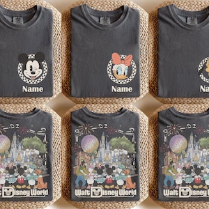Puede incluir: Una colecci&oacute;n de camisetas gris carb&oacute;n con gr&aacute;ficos de personajes de Disney. El frente muestra un emblema circular a cuadros con Mickey, Daisy o Pluto y el texto Name. La parte posterior muestra una escena detallada del parque Walt Disney World.