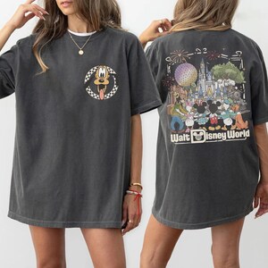 Puede incluir: Una camiseta gris carb&oacute;n de manga corta con un peque&ntilde;o gr&aacute;fico circular de Pluto en el pecho izquierdo. La parte posterior muestra una gran ilustraci&oacute;n colorida de personajes de Disney frente a un castillo con el texto Walt Disney World.
