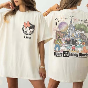 Puede incluir: Una camiseta color marfil con un peque&ntilde;o gr&aacute;fico de Minnie Mouse y el nombre Lisa en el pecho izquierdo. La parte posterior muestra una gran ilustraci&oacute;n colorida del castillo de Walt Disney World, fuegos artificiales y personajes.