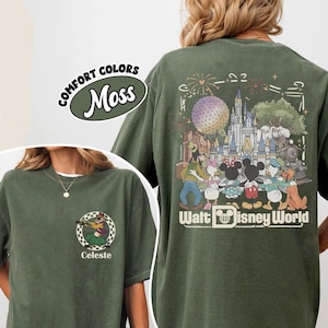 Puede incluir: Una camiseta verde musgo con un peque&ntilde;o gr&aacute;fico en el pecho de un personaje con falda hawaiana dentro de un c&iacute;rculo a cuadros con el nombre Celeste. La parte trasera muestra una gran ilustraci&oacute;n de personajes Disney en Walt Disney World.