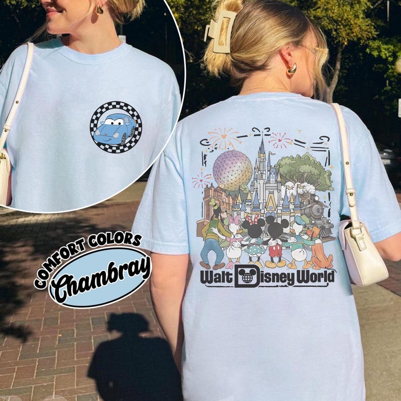 Puede incluir: Una camiseta azul claro con un peque&ntilde;o gr&aacute;fico circular en la parte delantera que muestra un coche azul dentro de un borde a cuadros. La parte trasera muestra una gran ilustraci&oacute;n de personajes Disney frente a un castillo y el texto Walt Disney World.