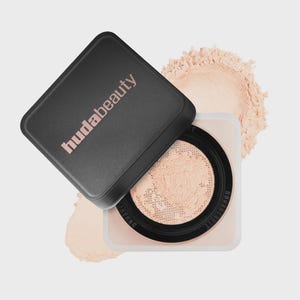 May include: A square cosmetic container with a black lid featuring the text hudabeauty in light pink. The base is clear with a black inner rim and a mesh sifter containing loose, light beige setting powder, with more powder visible behind it.