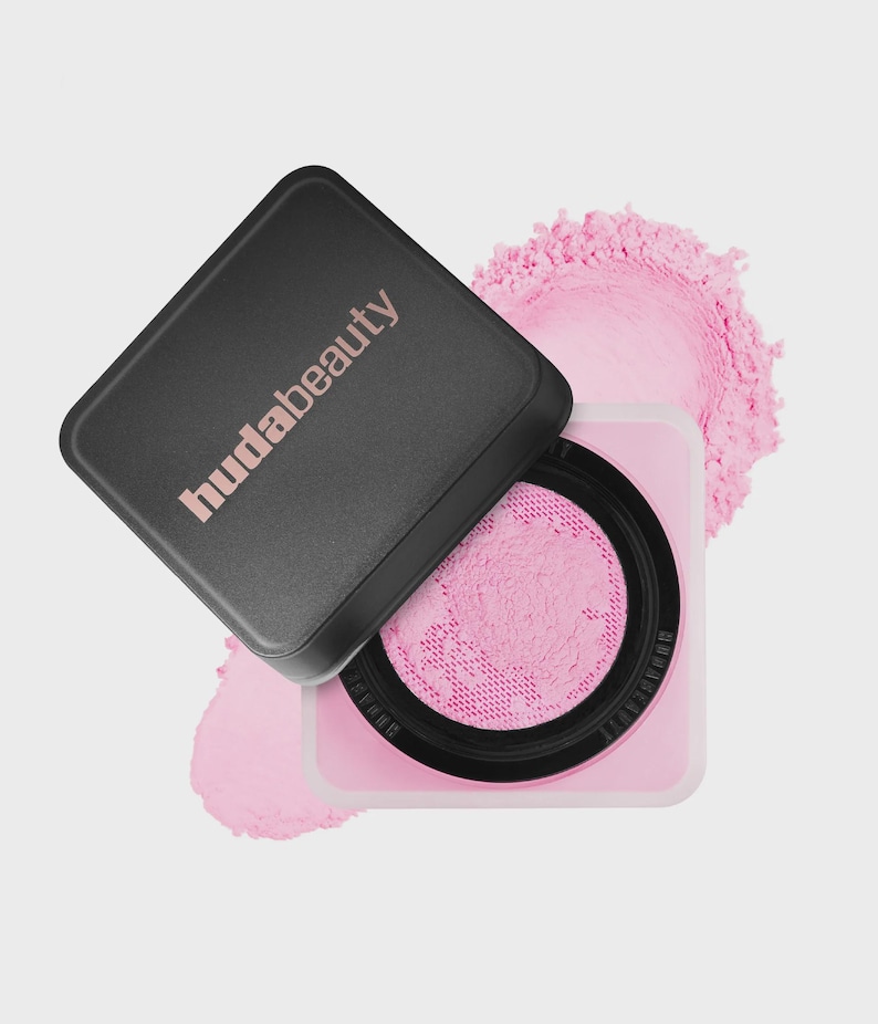 May include: A square cosmetic container with a black lid featuring the text hudabeauty in light pink. The base is light pink with a black circular insert containing a fine, bright pink loose powder visible through a mesh sifter screen.