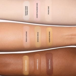 May include: Three arms display cosmetic powder swatches. Top row: Sugar Cookie Translucent, Cherry Blossom Cake, Pound Cake. Middle row: Peach Cupcake, Banana Bread, Kunafa Blondie. Bottom row: Kunafa Blondie, Cinnamon Bun, and Coco Truffle.