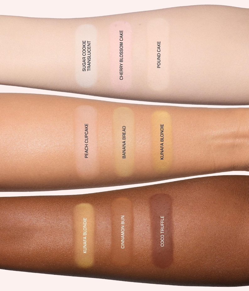May include: Three arms display cosmetic powder swatches. Top row: Sugar Cookie Translucent, Cherry Blossom Cake, Pound Cake. Middle row: Peach Cupcake, Banana Bread, Kunafa Blondie. Bottom row: Kunafa Blondie, Cinnamon Bun, and Coco Truffle.