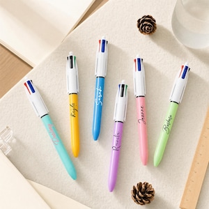May include: Six multi-color retractable ballpoint pens with white clips and tops. Each pen features a different colored barrel: light blue, yellow, blue, purple, pink, and light green. Each barrel is personalized with a name in black script.