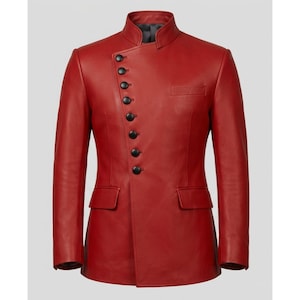 Puede incluir: Una chaqueta de color rojo vibrante con cuello mao alto y cierre frontal asimétrico asegurado por una fila de siete botones negros redondos. La prenda incluye dos bolsillos horizontales con solapa en la cintura y un bolsillo en el pecho.
