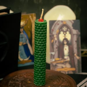 Peut inclure: Une bougie cylindrique verte avec un motif en nid d'abeille texturé sur sa surface. La bougie présente une mèche de couleur claire centrée au sommet, entourée d'un petit accent en cire rouge. La bougie est posée sur une base en bois circulaire.