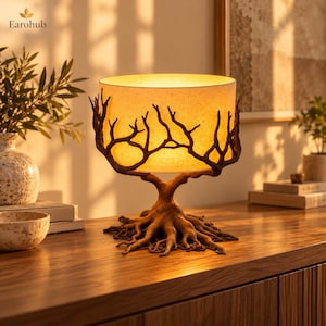 May include: A table lamp featuring a cylindrical beige fabric shade supported by a dark brown base sculpted to resemble tree roots and branches that extend upward to cradle the light source, emitting a warm, soft glow.