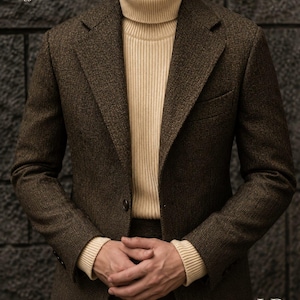 Peut inclure: Un blazer à motif chevrons marron foncé porté sur un pull à col roulé côtelé de couleur crème. Le blazer présente des revers crantés et une fermeture à un bouton. Le texte LB. est visible dans les coins supérieur gauche et inférieur droit.