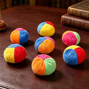May include: Seven small, round, plush balls, each featuring a segmented design with vibrant, multi-colored fabric panels in shades of red, blue, yellow, orange, and green. The soft, textured surface of each ball is divided into distinct sections.