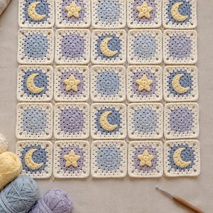 May include: A grid of twenty-five crocheted squares in shades of blue, purple, and cream. The squares feature alternating patterns of solid circles, yellow crescent moons, and yellow stars. Three skeins of yarn and a crochet hook are visible.