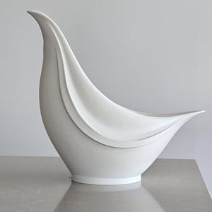 May include: A matte white ceramic vase with a bird-like silhouette, featuring a curved, elongated neck and a pointed tail. The surface displays fine, horizontal ribbed textures that follow the sweeping, organic contours of the vessel's form.
