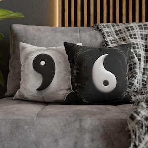 Könnte beinhalten: Zwei quadratische Dekokissen mit Yin-und-Yang-Motiv. Das linke Kissen ist weiß mit einer schwarzen Yin-Form und einer marmorierten Textur. Das rechte Kissen ist schwarz mit einer weißen Yang-Form und einem subtilen, wirbelnden Rauchmuster.