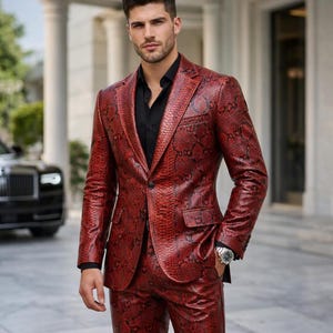 May include: A red blazer and matching trousers featuring a textured snakeskin pattern. The suit is worn over a solid black button-down shirt. The blazer has a notched lapel, a single front button closure, and two flap pockets on the front.