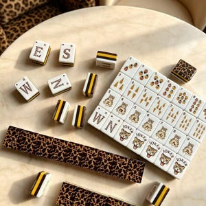 May include: A Mahjong set featuring white tiles with various designs including leopard print, black and yellow stripes, ladybugs, pine trees, and tiger faces. Some tiles display letters, numbers, and the word JOKER in black ink.