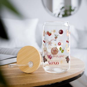 Könnte beinhalten: Ein durchsichtiges Glas mit Bambusdeckel und Glasstrohhalm. Das Glas ist mit bunten Symbolen bedruckt, darunter Erdbeeren, Kirschen, eine Discokugel, Herzen, eine Billardkugel sowie der Schriftzug "love you!" und "XOXO" in roter Schrift.