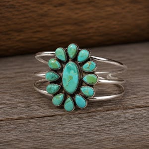 May include: A silver cuff bracelet featuring a central oval turquoise stone surrounded by twelve smaller teardrop-shaped turquoise stones arranged in a floral pattern. The bracelet has a triple-band design made of polished silver metal.
