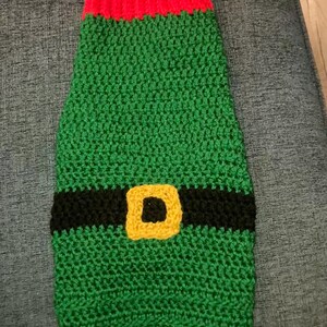 May include: Green and red crocheted dog sweater with a black belt and a yellow buckle.