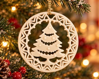 May include: A circular cream-colored ornament featuring a cutout design of a stylized Christmas tree in the center, surrounded by a wavy, openwork border. The ornament is suspended by a gold-colored cord and has a smooth, matte finish.