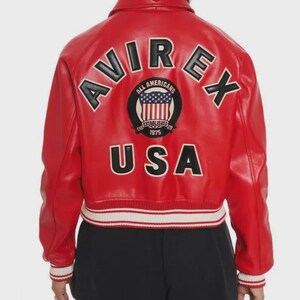 May include: A bright red leather jacket featuring the word AVIREX in large black letters across the upper back. Below this, a circular patch displays the American flag with the text ALL AMERICANS ESTABLISHED 1975. The word USA appears in black letters at the bottom, with white and red striped ribbed trim at the cuffs and waist.