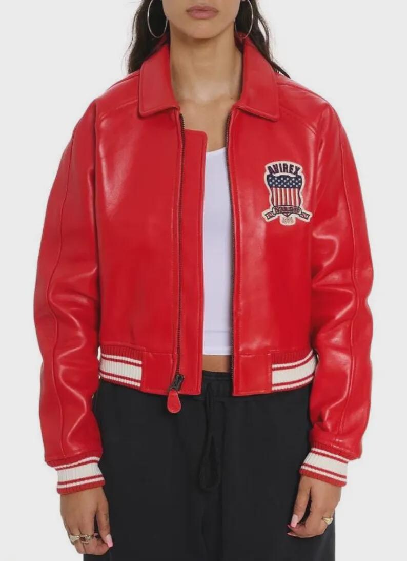 May include: A bright red leather jacket featuring a front zipper closure, a classic collar, and ribbed cuffs and hem with white stripes. On the left chest, there is a patch with the text Avirex, a shield graphic, and the words Established 1975.