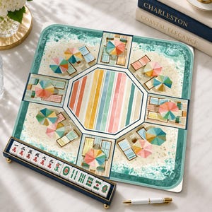 May include: A square mahjong mat featuring a beach scene with colorful umbrellas and lounge chairs surrounding a central striped octagon. A dark blue tile rack displays white mahjong tiles with red and green Chinese characters and symbols.