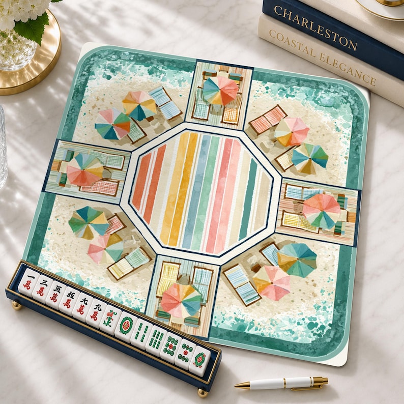 May include: A square mahjong mat featuring a beach scene with colorful umbrellas and lounge chairs surrounding a central striped octagon. A dark blue tile rack displays white mahjong tiles with red and green Chinese characters and symbols.