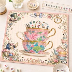 May include: A square decorative mat featuring a stack of three ornate teacups filled with mahjong tiles. The design includes a rabbit, a top hat, a pocket watch, playing cards, and floral patterns in shades of pink, blue, and gold on a cream background.